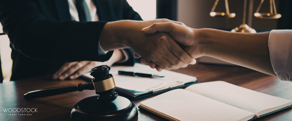 Handshake over desk with gavel and scales, symbolising legal agreement – Woodstock Legal Services.