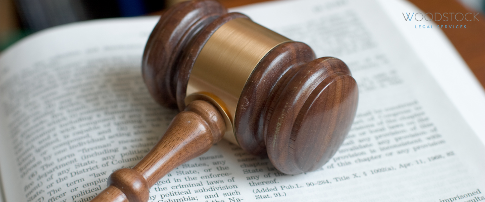 A wooden judge’s gavel resting on an open law book, with the Woodstock Legal Services logo visible