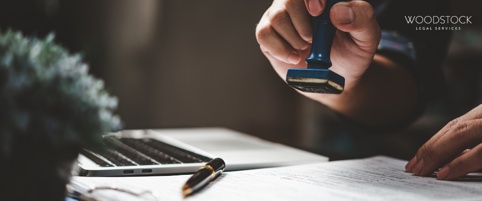 Close-up of a hand stamping a legal document with a laptop and pen on the desk, representing Woodstock Legal Services