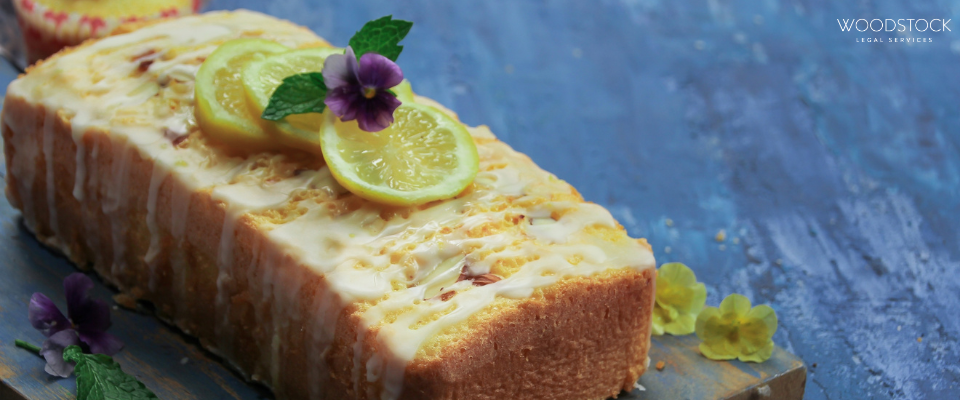 A glazed lemon drizzle loaf cake topped with thin lemon slices, mint leaves, and edible flowers,