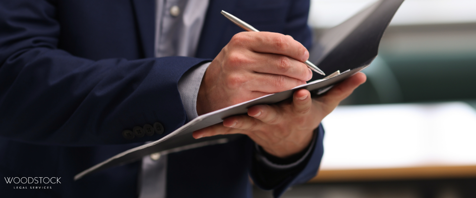 A professional in a suit writing notes on a clipboard, symbolising legal documentation, client meetings, and workplace advisory services by Woodstock Legal Services.