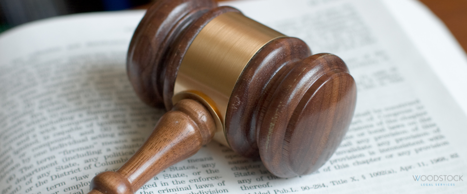 A wooden judge’s gavel resting on an open law book, with the Woodstock Legal Services logo visible in the top right corner.