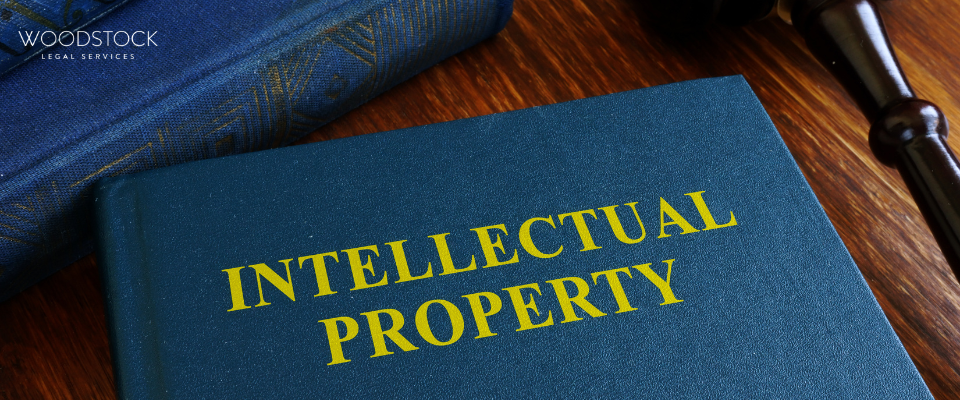 A blue book titled ‘Intellectual Property’ placed on a wooden desk beside a gavel and another book, with the Woodstock Legal Services logo in the top left corner