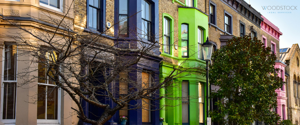 A row of colourful Victorian terraced houses in blue, green, and pink, by trees and a traditional