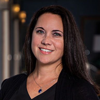 A woman wearing a black shirt and a blue necklace is smiling for the camera.