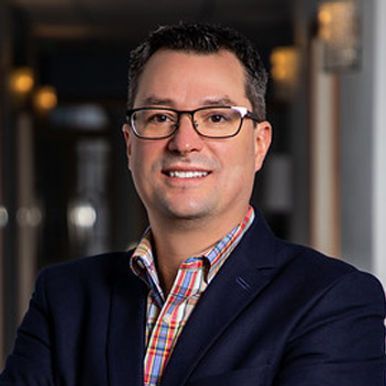 A man wearing glasses and a suit is smiling for the camera.