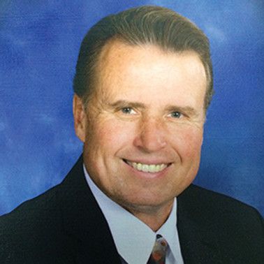 A man in a suit and tie is smiling in front of a blue background.