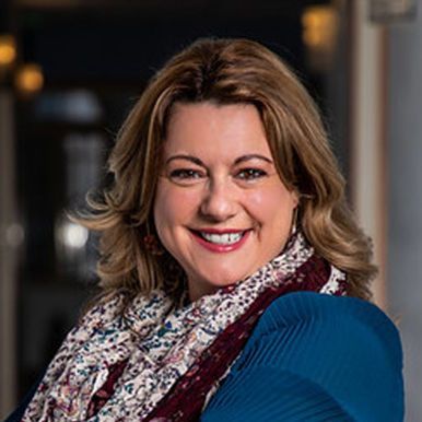 A woman wearing a scarf and a blue shirt is smiling for the camera.