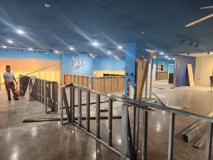 A person walks through an indoor construction site with metal wall frames, polished concrete floors, and blue ceilings.