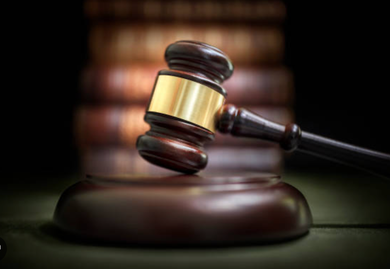 A wooden judge 's gavel is sitting on a wooden block in front of a stack of books.