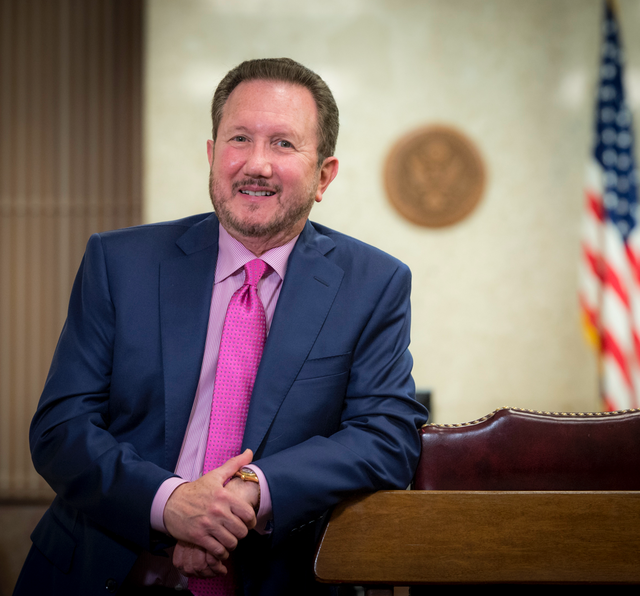 A man in a suit and pink tie is leaning on a podium