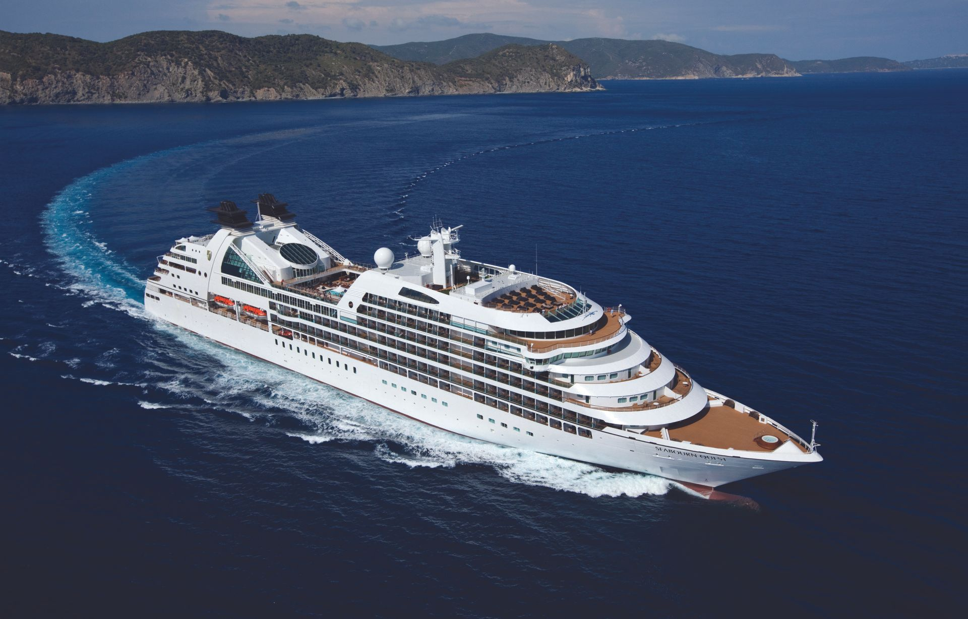White cruise ship sailing on deep blue water near a coastline and distant hills