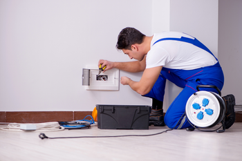 A man is kneeling on the floor working on a wall.