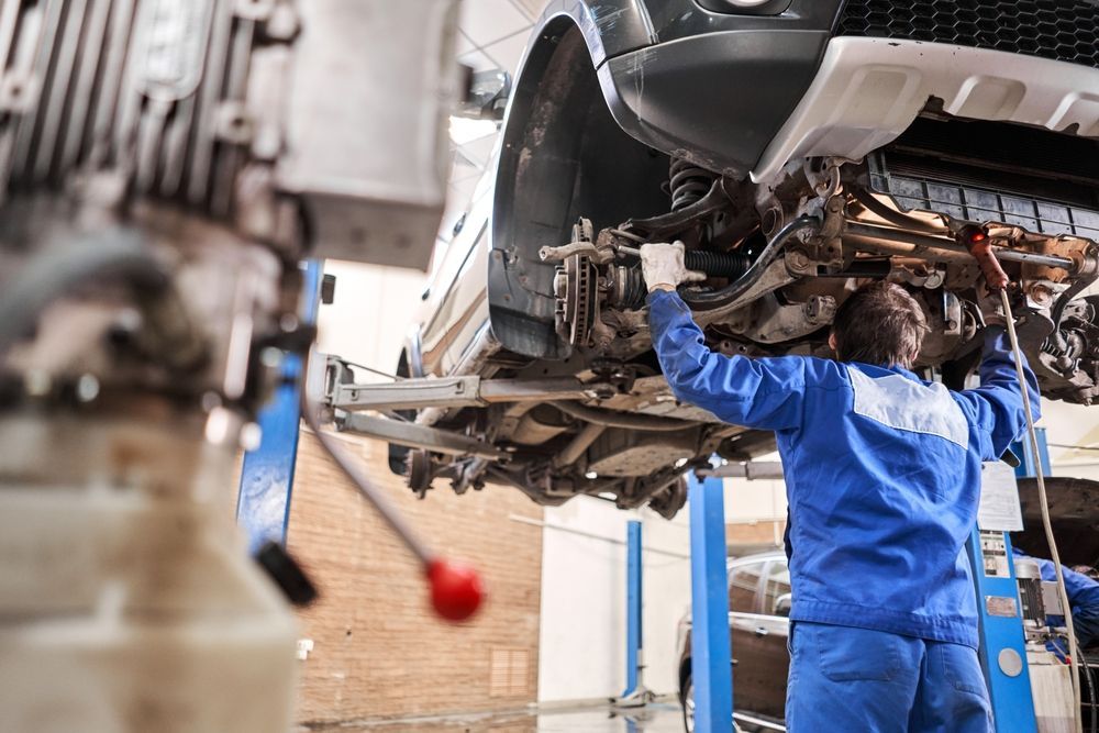 Mechanic in Blue Uniform Works on a Car Raised on a Lift Inside a Garage — Argenton Automotive Repairs In Boolaroo, NSW