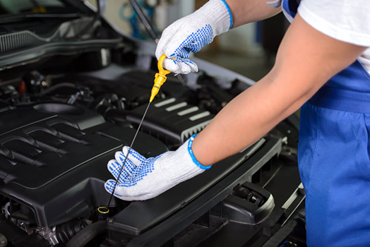 Mechanic in Blue Overalls Checking Car Oil With a Yellow Dipstick — Argenton Automotive Repairs In Boolaroo, NSW