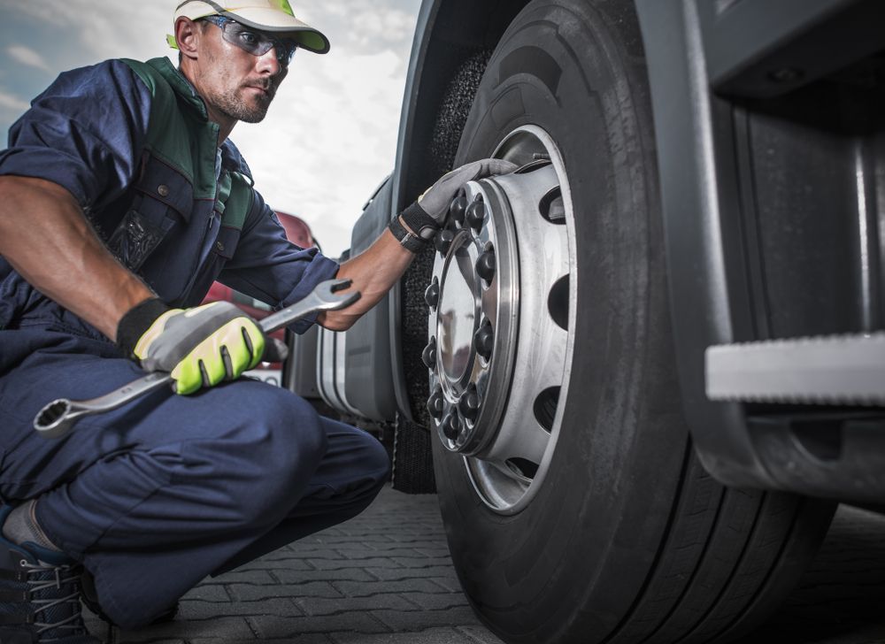 Mechanic in Blue Overalls, Using a Wrench on a Truck Tire, Outdoors — Argenton Automotive Repairs In Boolaroo, NSW