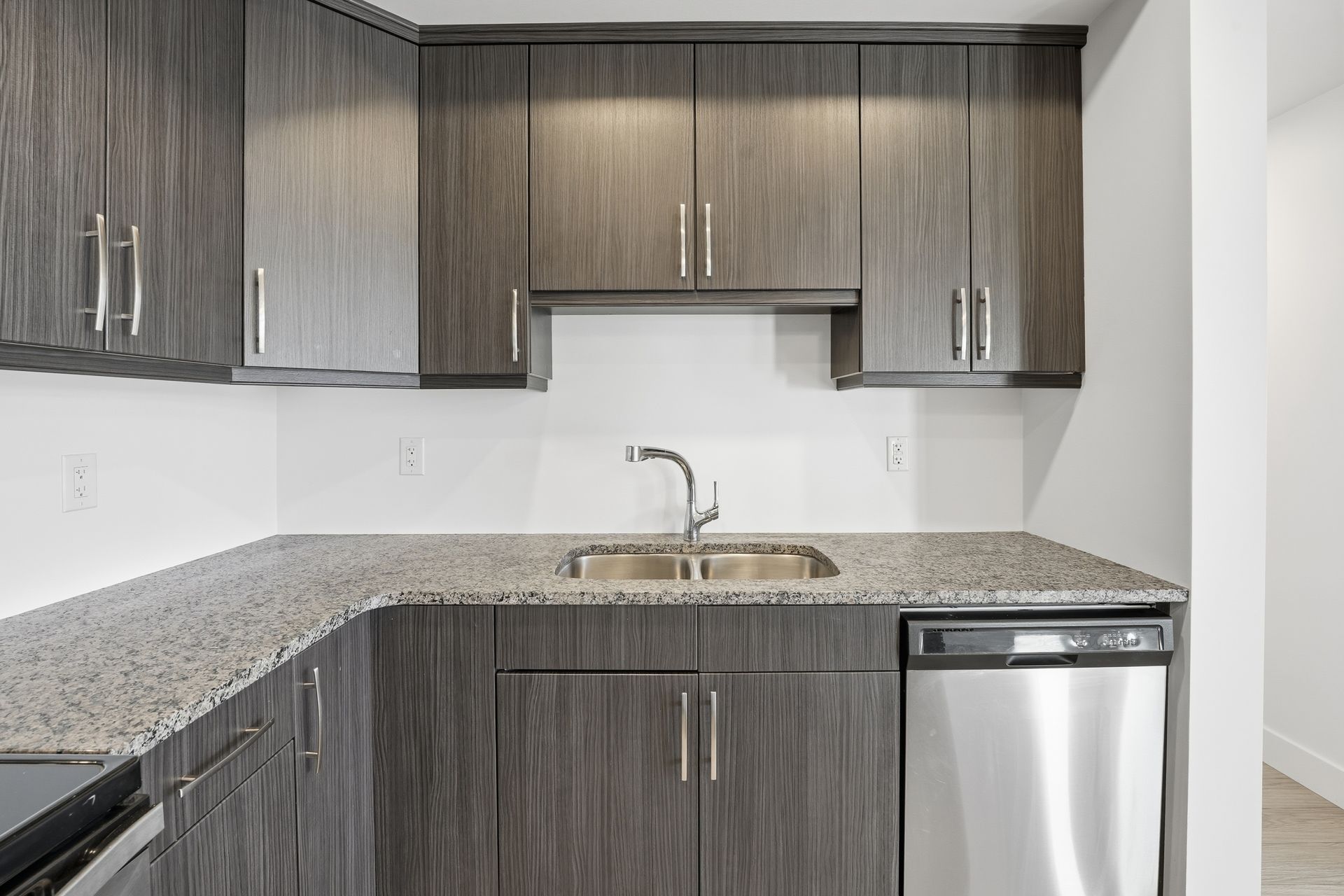 Modern kitchen with dark wood cabinets, granite countertop, stainless steel sink and appliances.