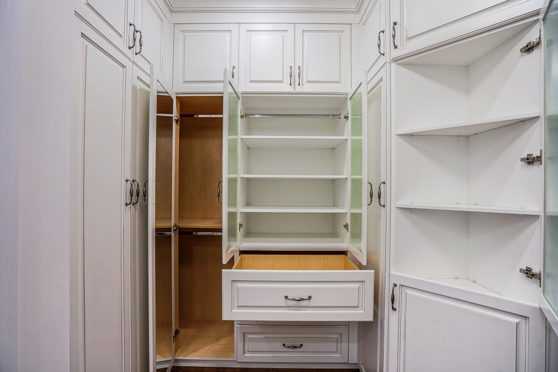 A walk in closet with white cabinets and drawers and a pull out drawer.