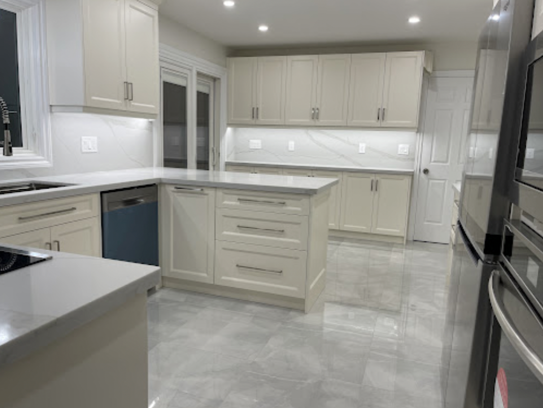 A modern, bright kitchen featuring cream-colored cabinets, light gray countertops, tiled flooring, and stainless appliances.