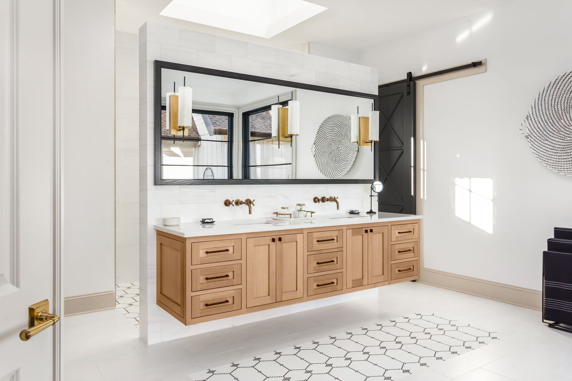 A modern bathroom with a floating light-wood vanity, white marble wall, long rectangular mirror, and black barn door.