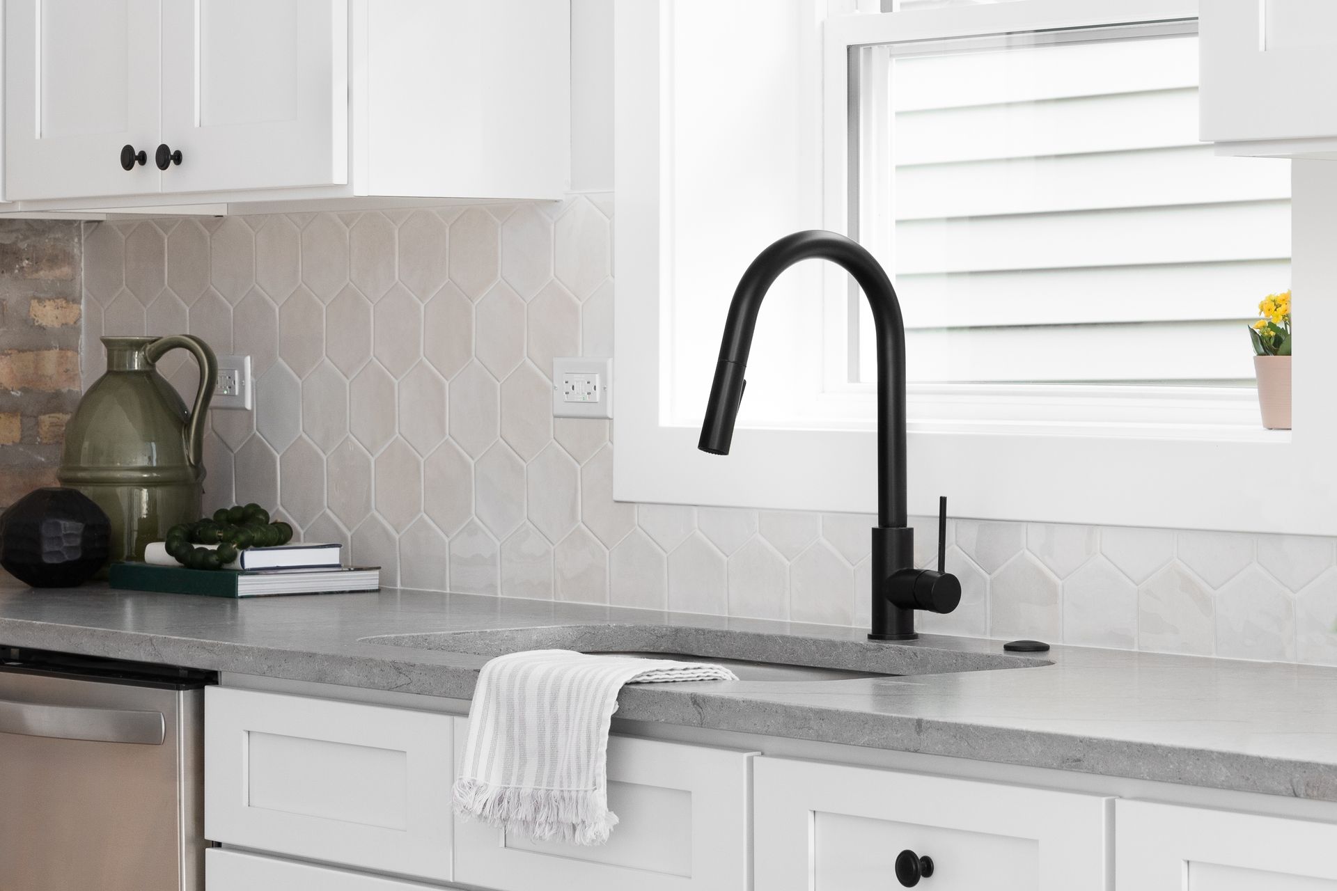 Modern kitchen with black faucet, light gray countertop, white cabinets, and patterned tile backsplash.