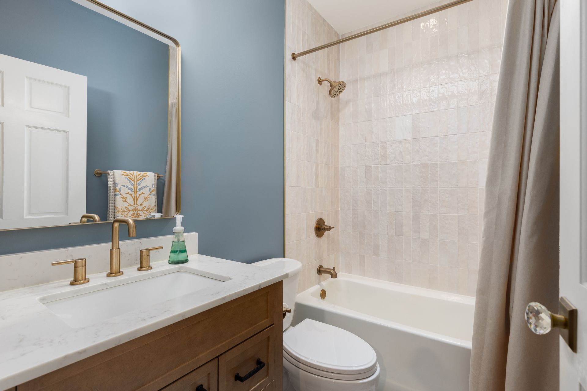 A modern bathroom with a wood vanity, white marble countertop, blue walls, a mirror, and a tiled shower-tub combo.