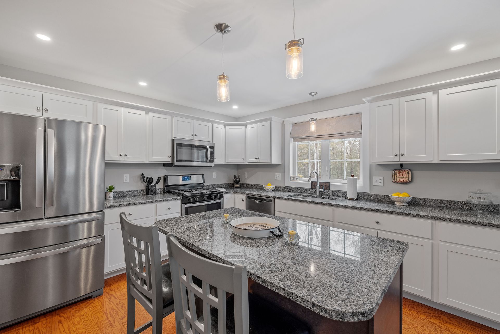A modern kitchen with white cabinets, speckled granite countertops, a center island with gray chairs, and stainless steel.