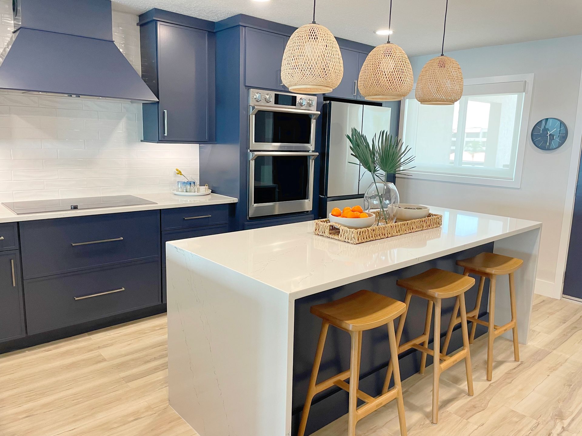 A modern kitchen with navy blue cabinets, white countertops, a large center island, and three light-wood bar stools.