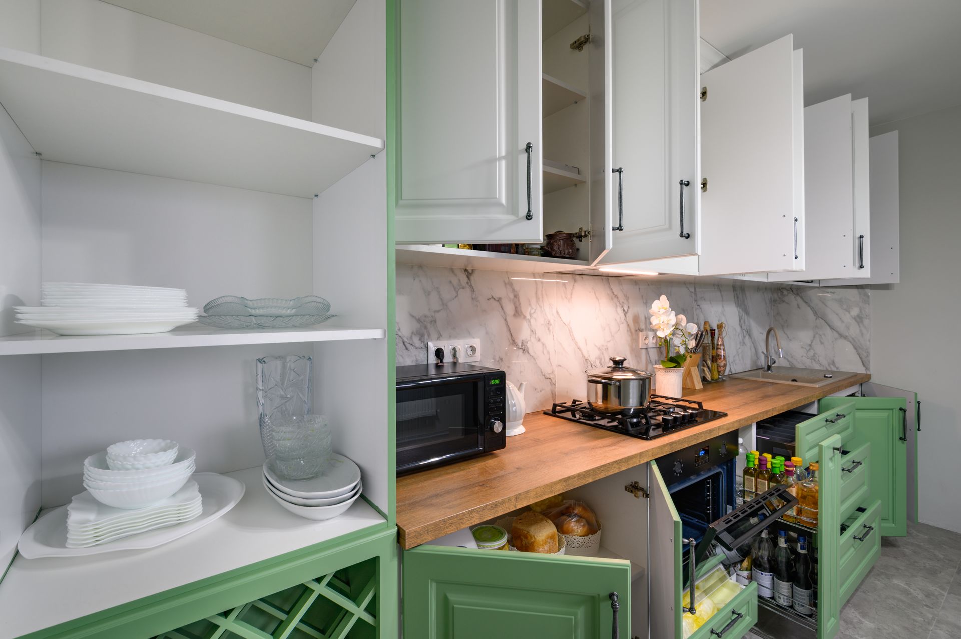 Green and white kitchen with open cabinets, shelves holding dishes, countertop with appliances.