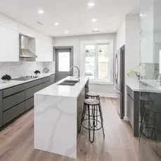 Modern kitchen with a white quartz island, gray cabinets, and hardwood floors.