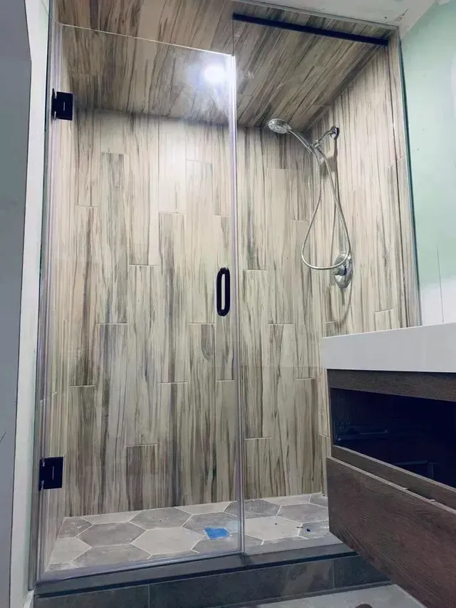 Shower with glass door, brown wood-look tile, dark hardware, and silver shower head.