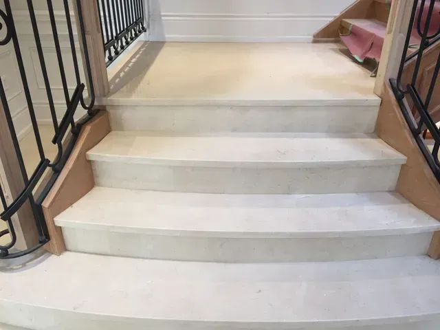 Limestone staircase with black wrought iron railing and wooden accents.