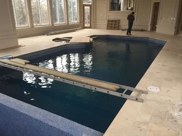 Indoor pool with blue water and tiled edges, surrounded by unfinished flooring. A person stands nearby.