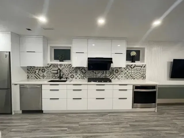 Modern white kitchen with stainless steel appliances, black accents, and patterned backsplash.