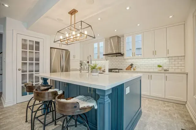 Modern kitchen with a blue island, white cabinets, and a chandelier.