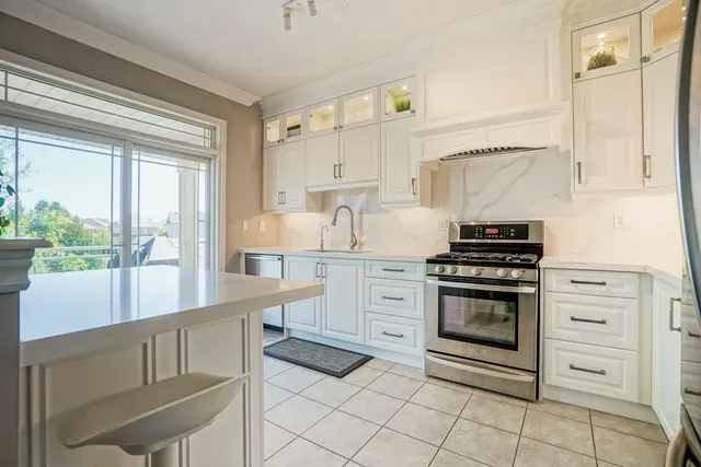 White kitchen with stainless steel appliances, marble backsplash, and a breakfast bar.