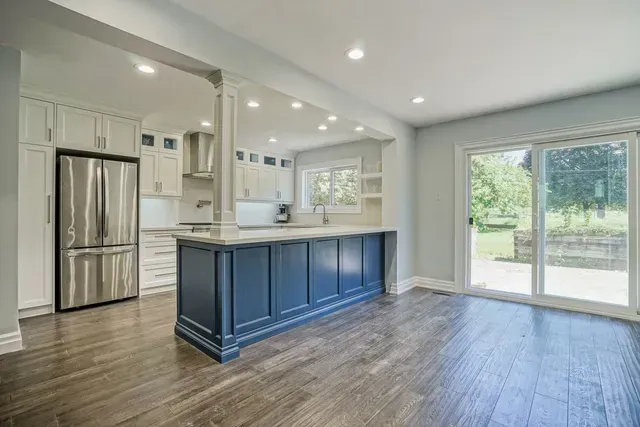 Spacious kitchen with blue island, stainless steel fridge, and sliding glass doors.