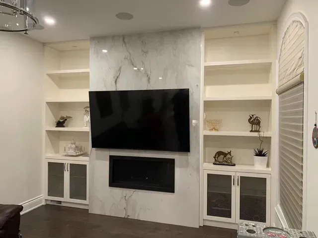 Built-in entertainment center with marble accent, flat-screen TV, fireplace, and shelving.