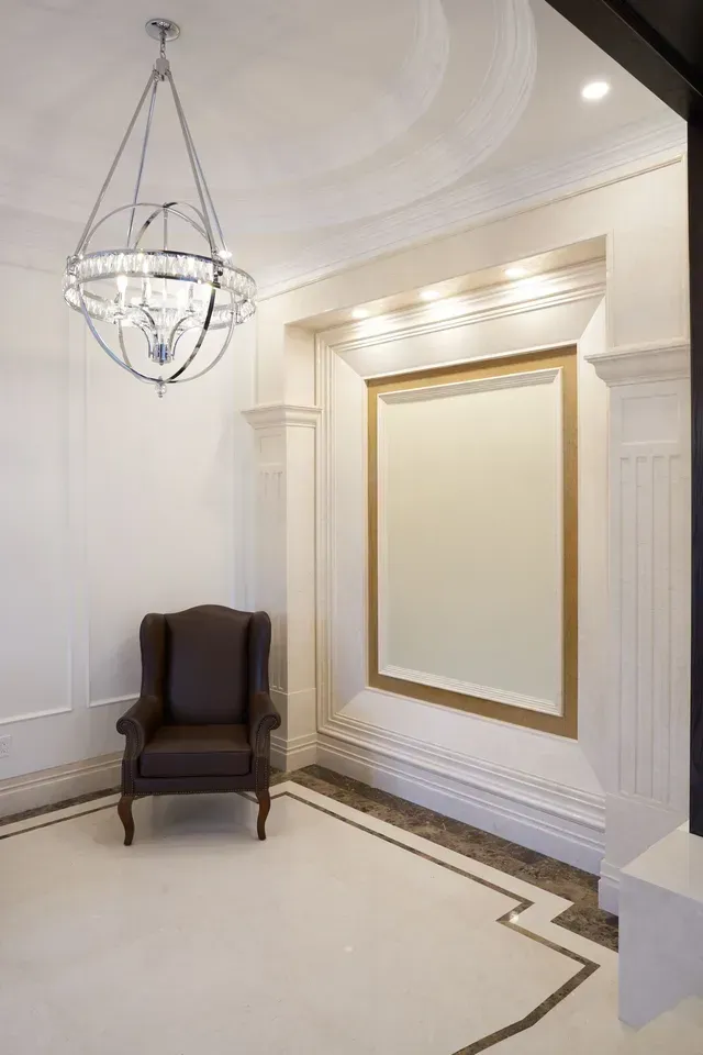 Elegant entryway with white walls, chandelier, brown armchair, and large mirror.