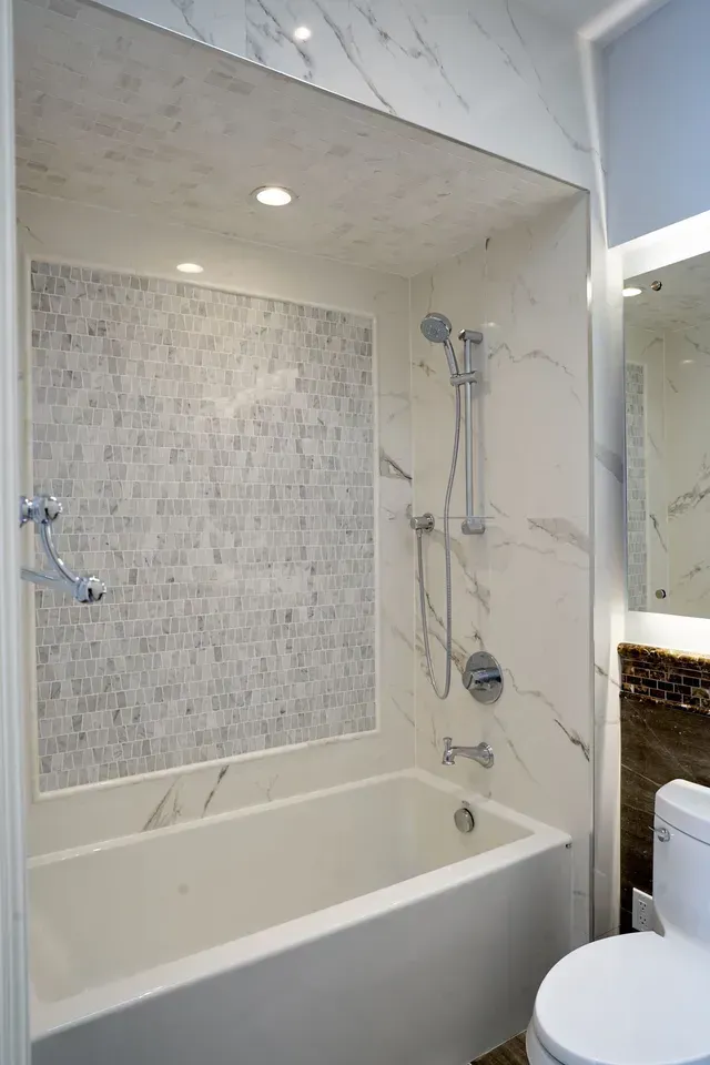 White modern bathroom with a tub, mosaic tile accent, and shower fixtures.