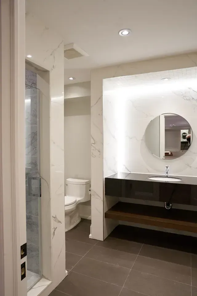 Modern bathroom with shower, toilet, and vanity. Gray floor, white marble walls, and round mirror.