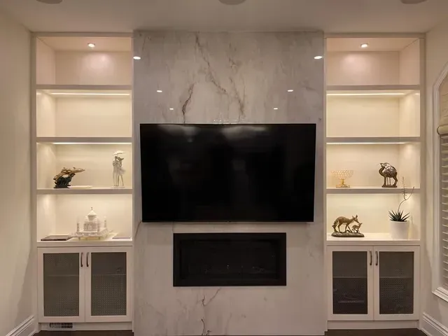 Built-in shelving flanking a marble-covered fireplace and TV. Shelves lit, with decorative objects.