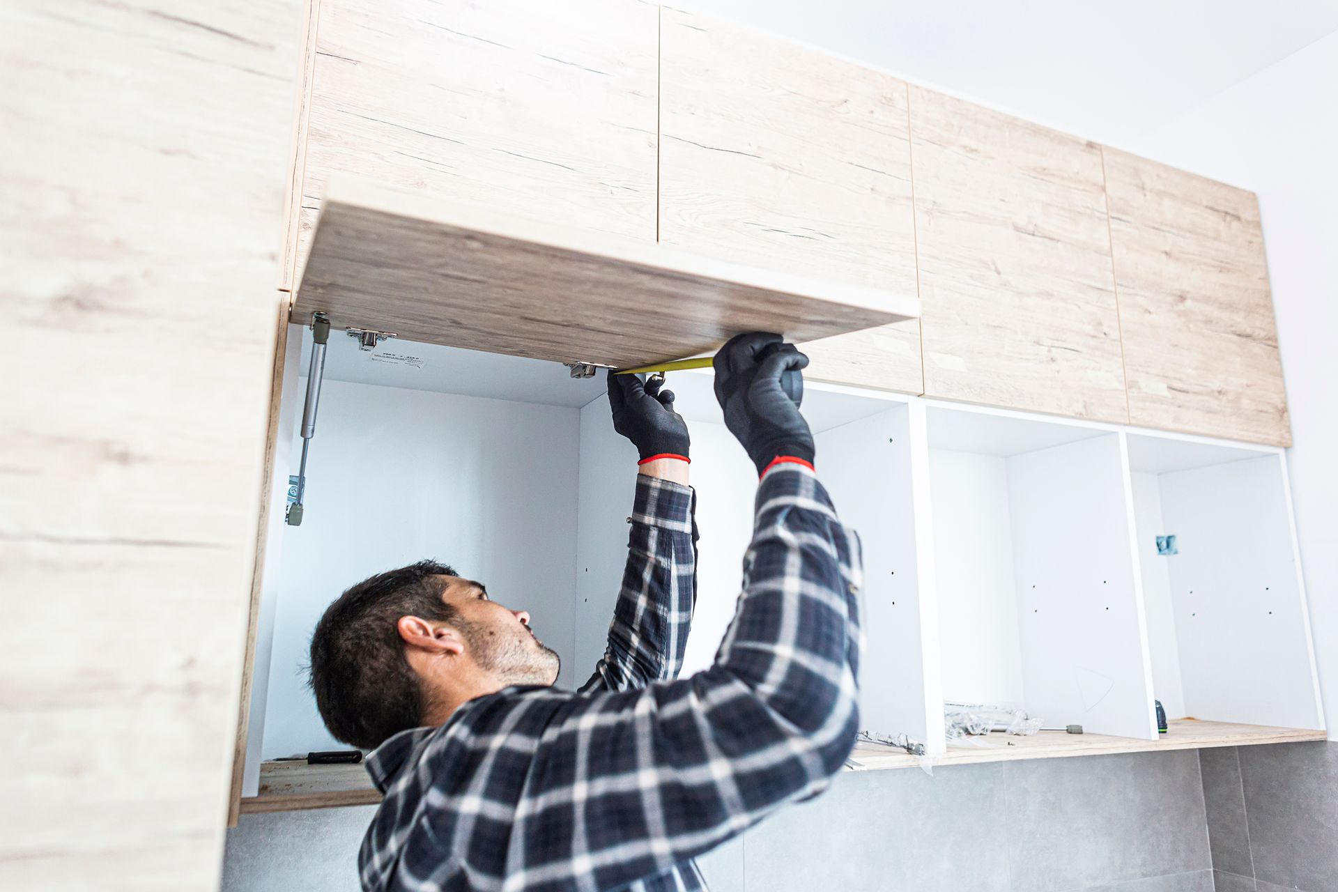 A man is measuring a cabinet with a tape measure in a kitchen.