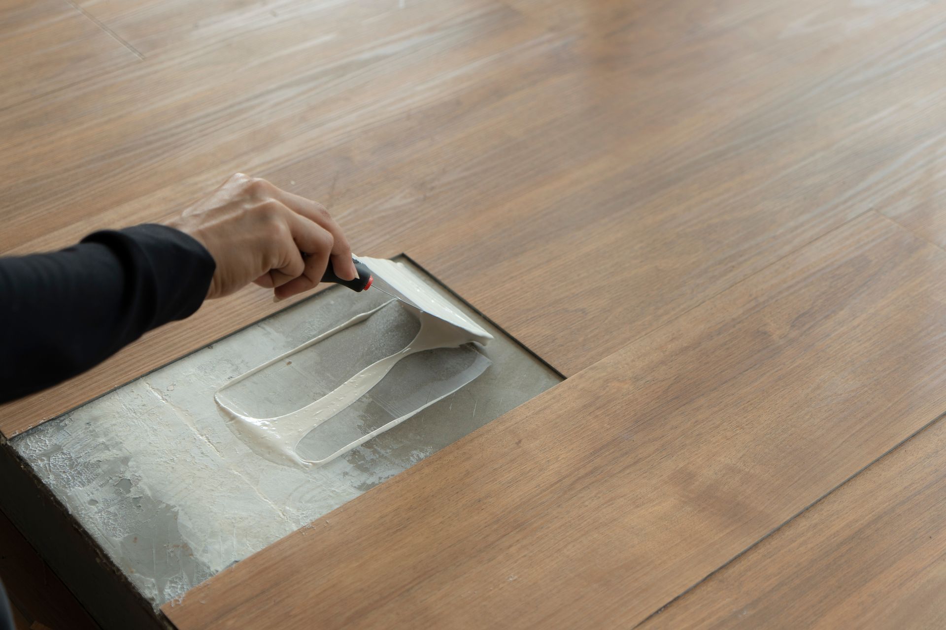 A person is applying glue to a wooden floor with a spatula.