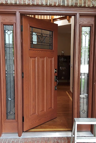 A wooden door with a stained glass window is open to a living room.