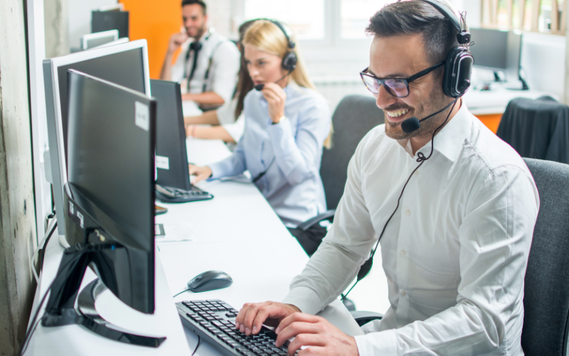 Call center staff wearing headsets working at computers in a bright office