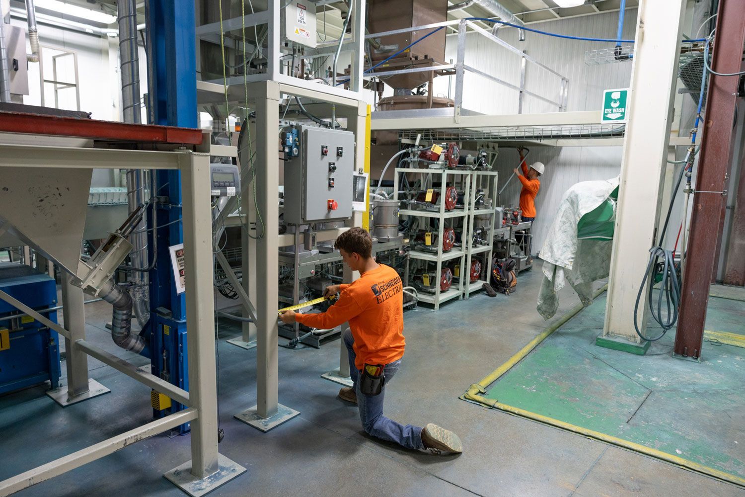 A man in an orange shirt is working on a machine in a factory.