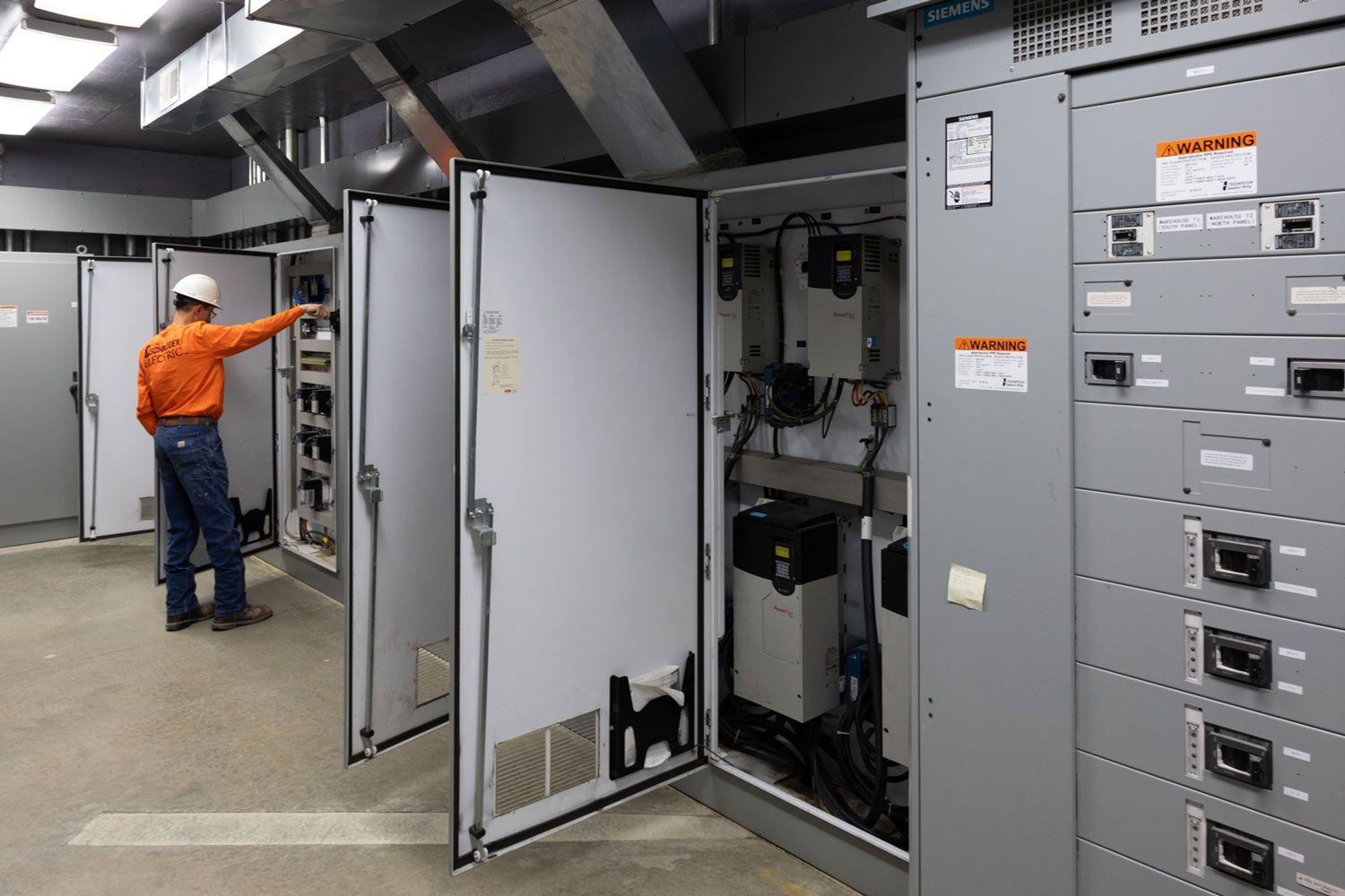 A man in an orange shirt is working on a electrical panel