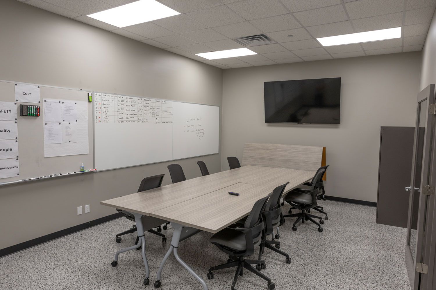 A conference room with a long table and chairs and a flat screen tv on the wall.