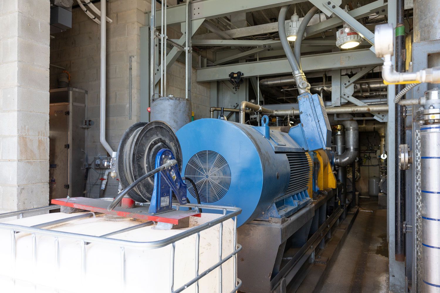 A large blue machine is sitting in a factory next to a white container.